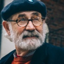 Headshot of a bearded elderly man wearing glasses and a beret